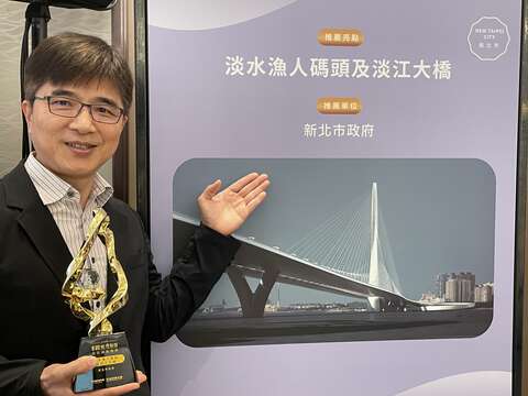 新北市观光旅游局庄荣哲副局长持「最佳国旅创新奖」奖盃，於淡江大桥主题背板前合影。