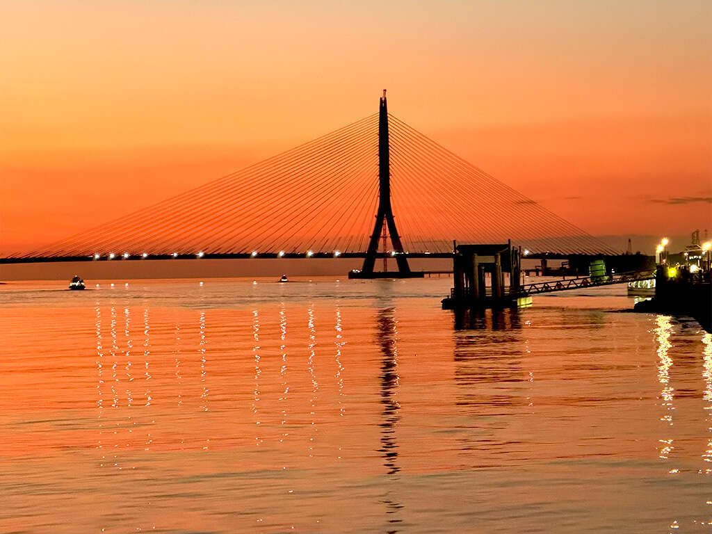 夕照映照淡江大橋與水岸景致，橘紅天色與橋體光影交織，呈現迷人河口風光。