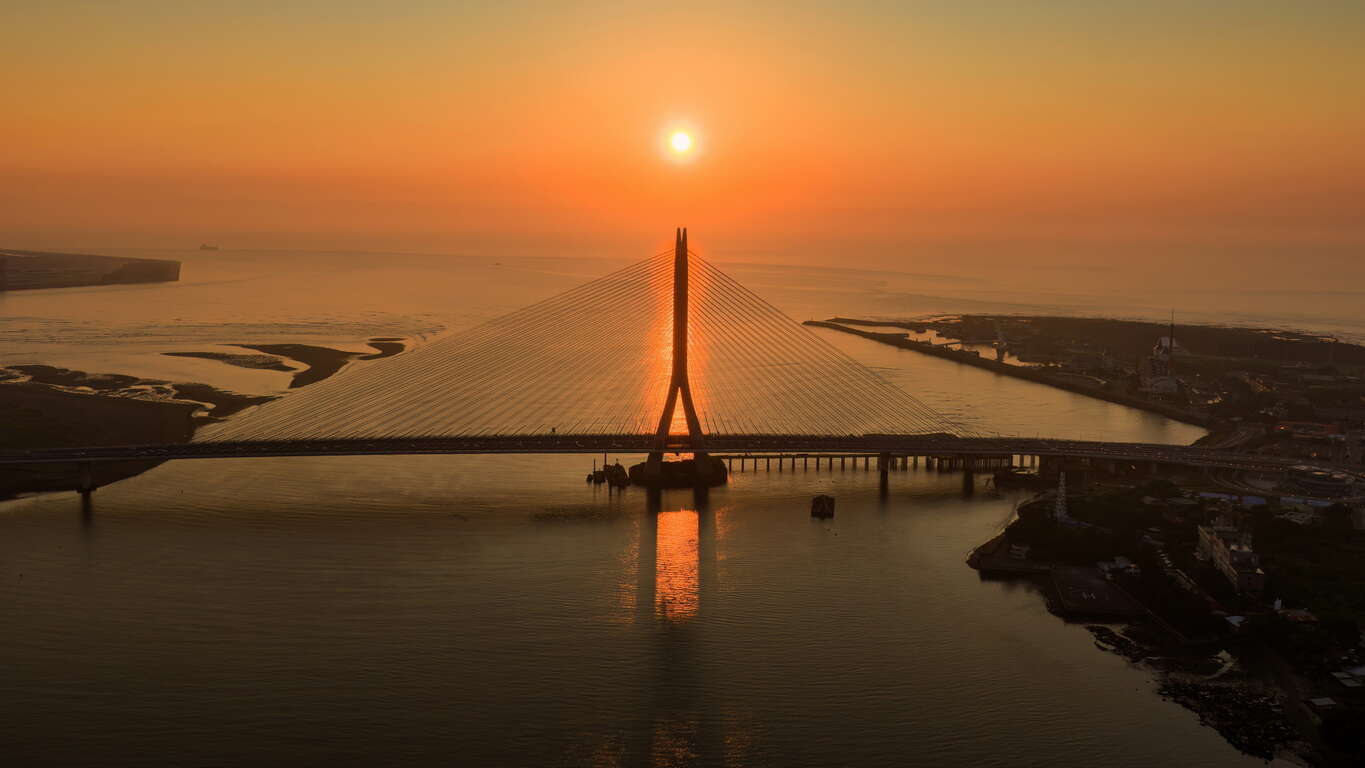淡水河口的金黄夕照与宏伟的淡江大桥巧妙相遇，桥塔的俐落剪影与波光 粼粼的水面勾勒出专属淡八地区的崭新观光地标。