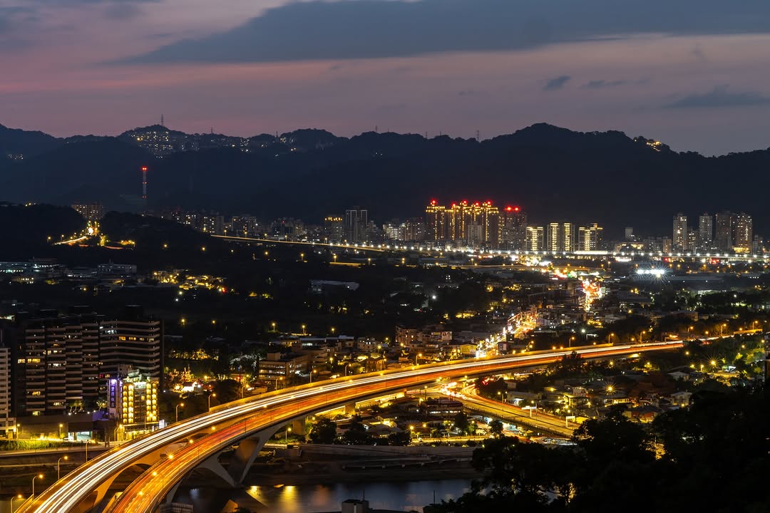 夕陽餘暉悄悄落下，城市的萬家燈火接連點亮，從高處俯瞰，蜿蜒的快速道路宛如一條耀眼的金色流光，穿梭在繁華的夜色之中