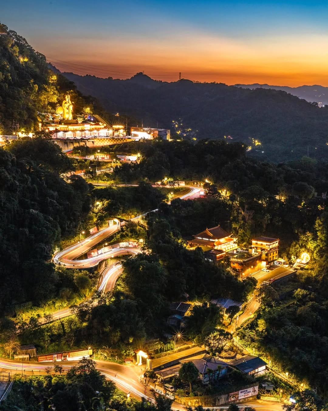 那道道蜿蜒的流光車軌穿梭在靜謐的山林間，遠方莊嚴的土地公巨像在霞光中守護著萬家燈火，彷彿是夜空與大地共同編織出最魔幻的詩篇